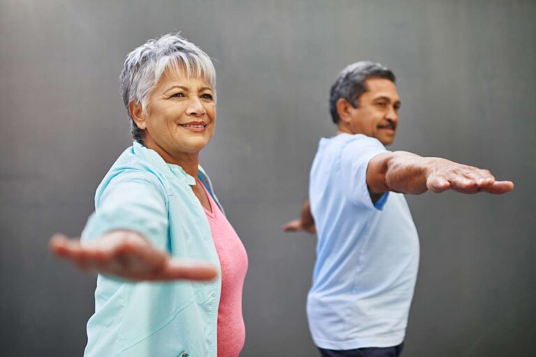Two older adults stand in a balance form during yoga