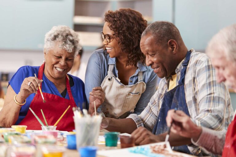 Three African American older adults smile together, wearing aprons at a painting class