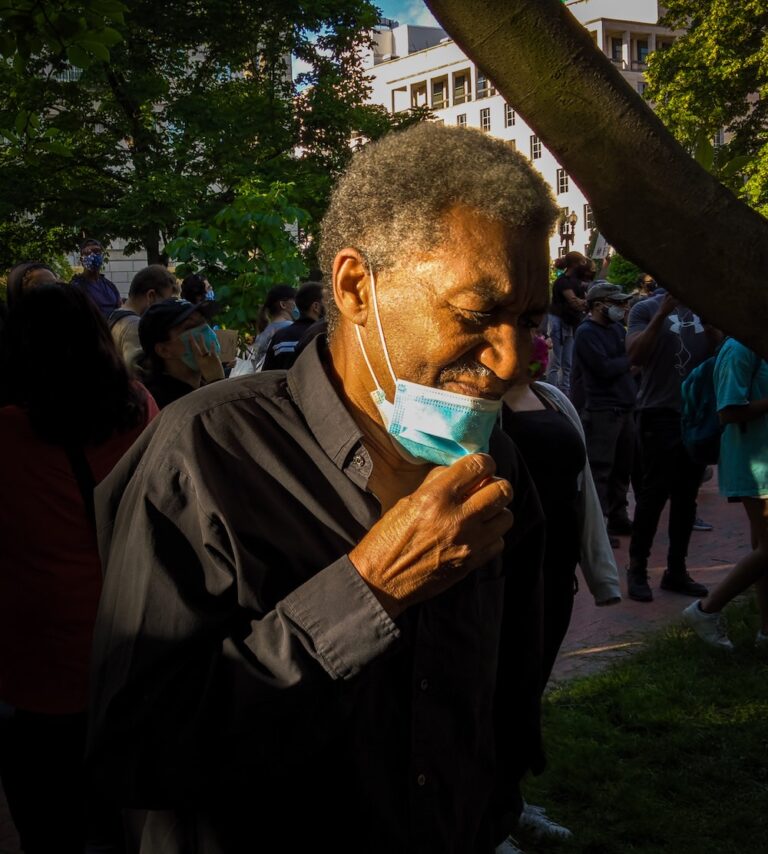 An older African American adult steps aside to take off his mask for a moment