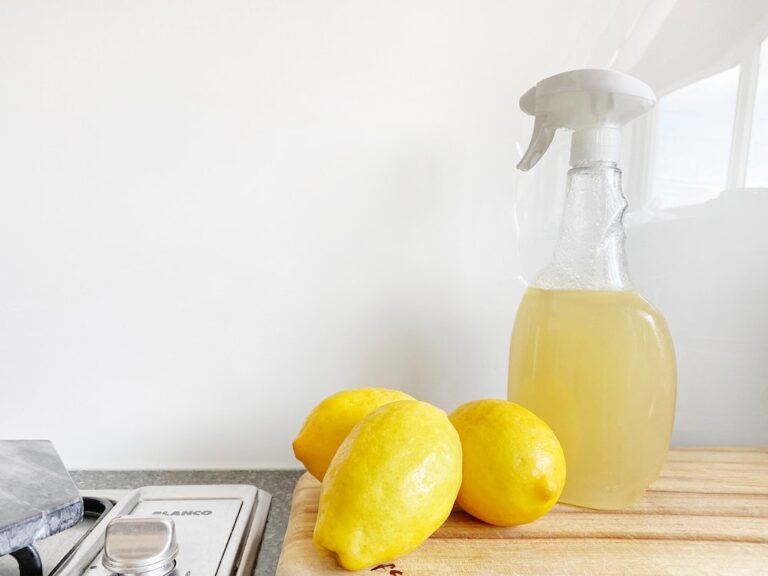 A clear plastic spray bottle filled with yellow fluid. Lemons sit on the countertop next to the bottle
