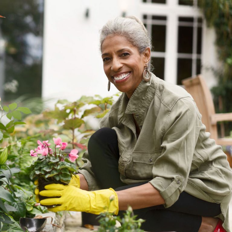 An older African American woman smiling while holding flowers she is about to plant in her garden