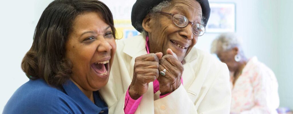 Two African American women embrace and smile. One is an adult and one is an older adult