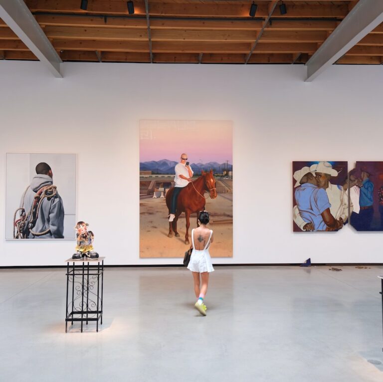 A girl stands in front of a series of paintings on a gallery wall
