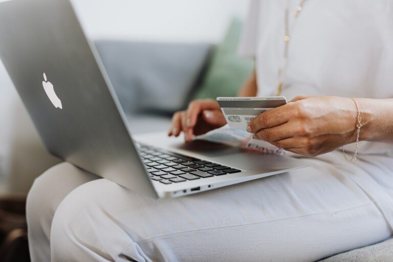 A person with a laptop on their lap is holding a credit card ready to type the numbers in to buy something online.